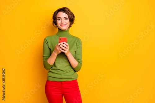 Portrait of positive cheerful girl use cellphone text type social network news chatting wear good looking clothing isolated over yellow color background