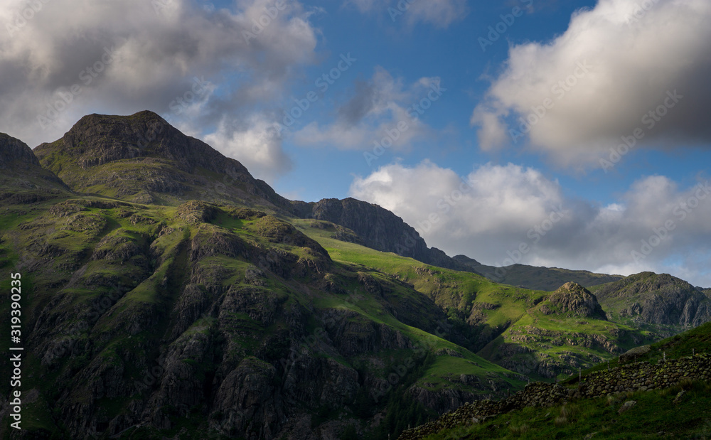 Stormy skies and a bright sun trace light over The Langdale Pikes in the English Lake District Stormy skies and a bright sun trace light over The Langdale Pikes in the English Lake District