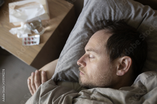 Man lying sick in bed with tissue box, medicine and glass of water