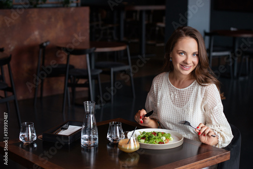 Smiling woman eats vegetarian salad in cafe