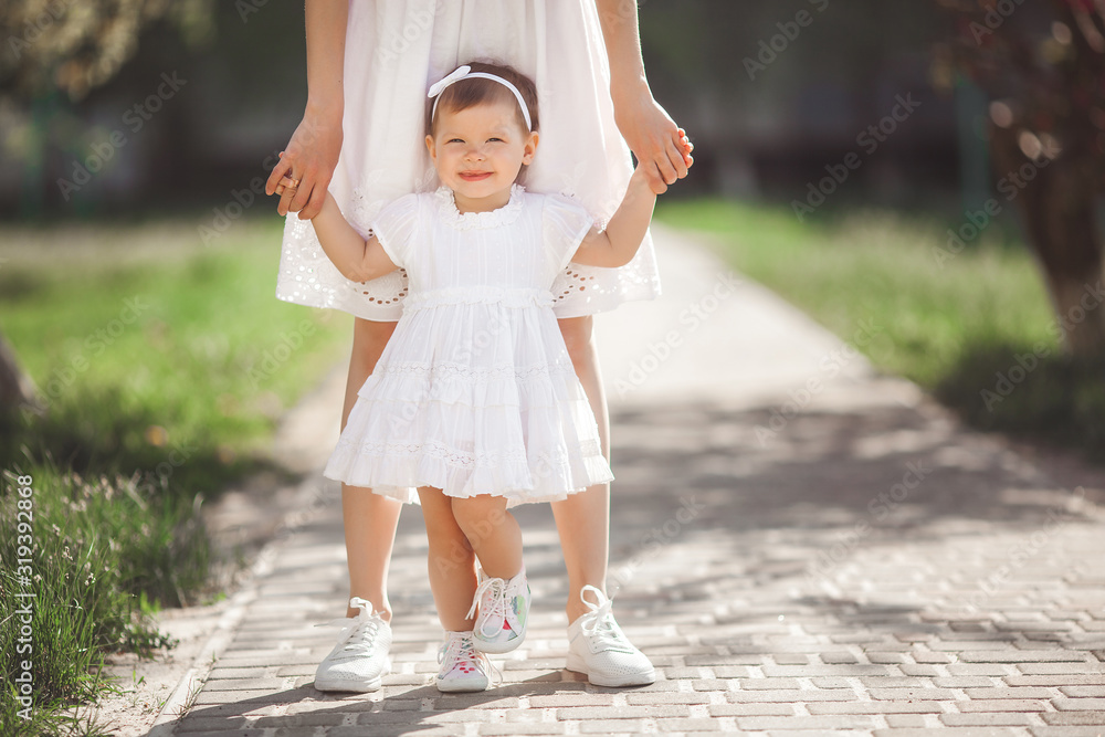 Fototapeta premium Young pretty mother walking on spring garden with her little cute daughter. Mom and child in spring flowers having fun. Family together outdoors.