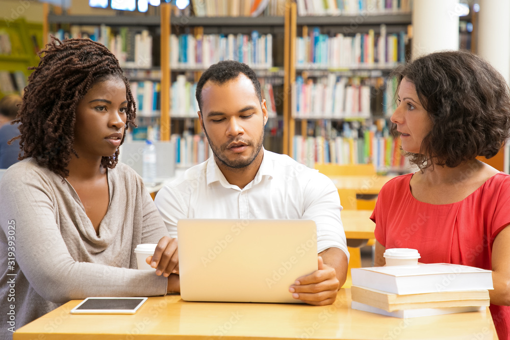 Front view of thoughtful people working at library. Focused students studying with laptop at library. Education concept Front view of thoughtful people working at library. Focused students studying with laptop at library. Education concept