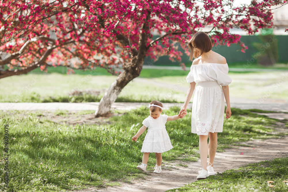 Young pretty mother walking on spring garden with her little cute daughter. Mom and child in spring flowers having fun. Family together outdoors. Young pretty mother walking on spring garden with her little cute daughter. Mom and child in spring flowers having fun. Family together outdoors.