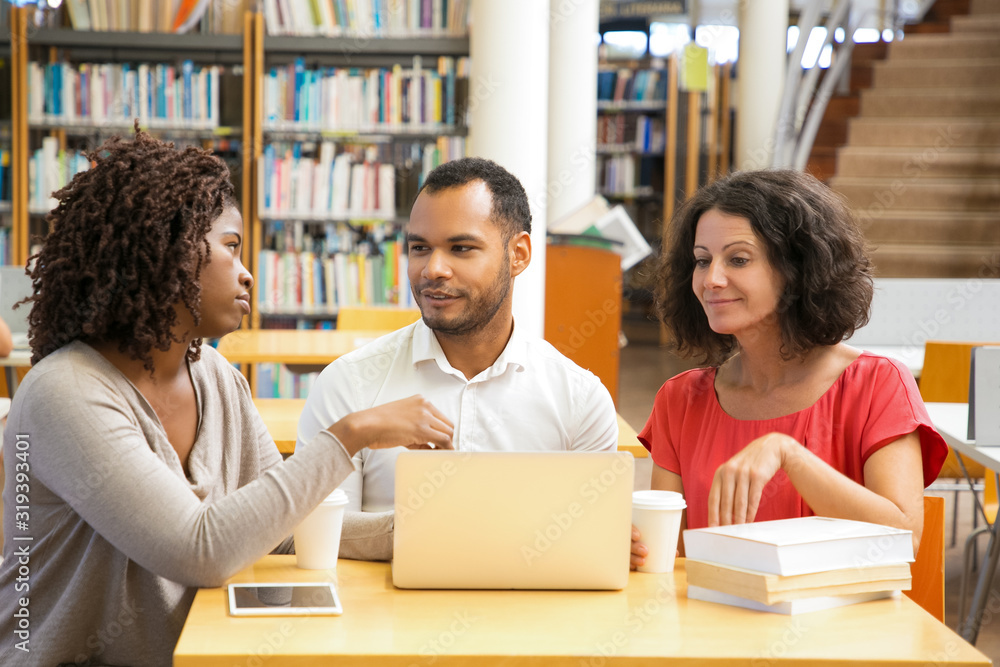 Front view of smiling people talking at library. Cheerful adult students studying with laptop at library. Education concept Front view of smiling people talking at library. Cheerful adult students studying with laptop at library. Education concept