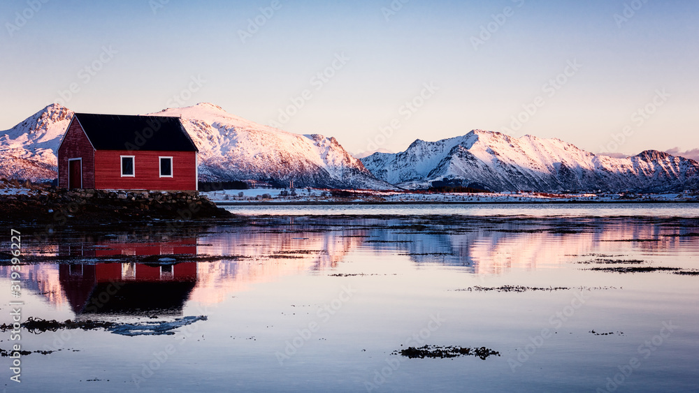 Amazing winter landscape with red rorbu, traditional scandinavian fishing house, snowy mountains in sunset light, blue sky and reflection in water, Lofoten Islands, Norway. Outdoor travel background Amazing winter landscape with red rorbu, traditional scandinavian fishing house, snowy mountains in sunset light, blue sky and reflection in water, Lofoten Islands, Norway. Outdoor travel background