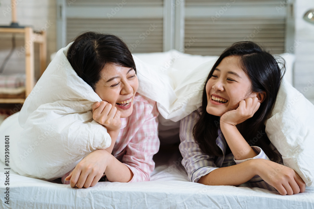 two asian korean best friends tell secrets in bed. Group of pretty young women in pajamas lying and talking under white blanket in cozy bedroom. beautiful female laughing cheerful chatting together two asian korean best friends tell secrets in bed. Group of pretty young women in pajamas lying and talking under white blanket in cozy bedroom. beautiful female laughing cheerful chatting together