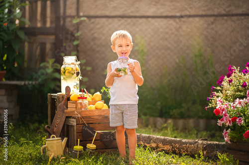 Boy sells homemade lemonade close-up and copy space. The boy in the summer makes homemade lemonade. Children's games with lemonade in the backyard.