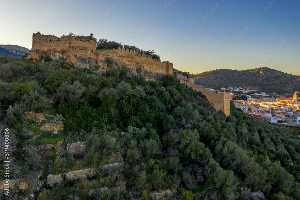 Aerial view of Corbera medieval Gothic castle in ruins on a hilltop near the coast with walls and a standalone tower in Spain 