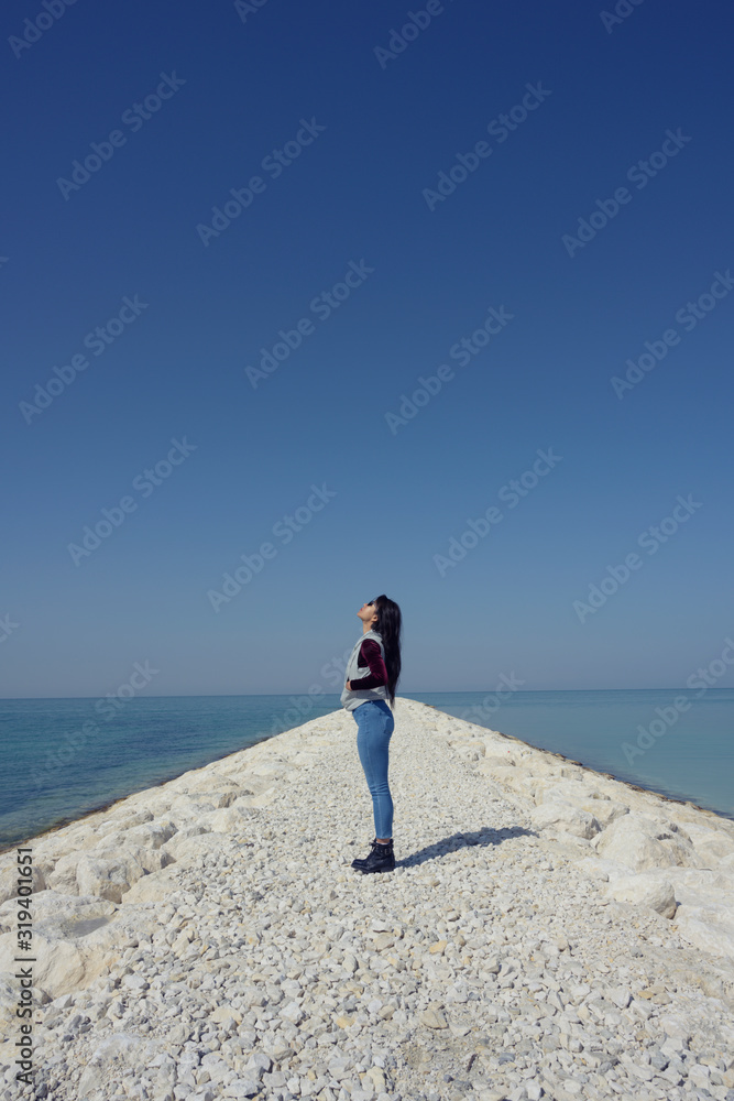 Woman wearing sunglass standing on seashore look up over blue sky background, Bahrain