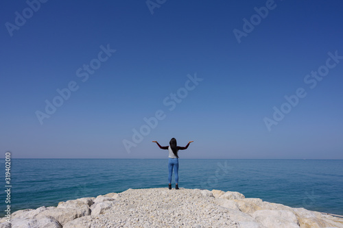 Woman standing on the seashore hands up over blue sky background, Bahrain.