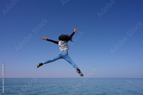 Woman open arms and legs jumping on the air over sea view and blue sky background, Bahrain.