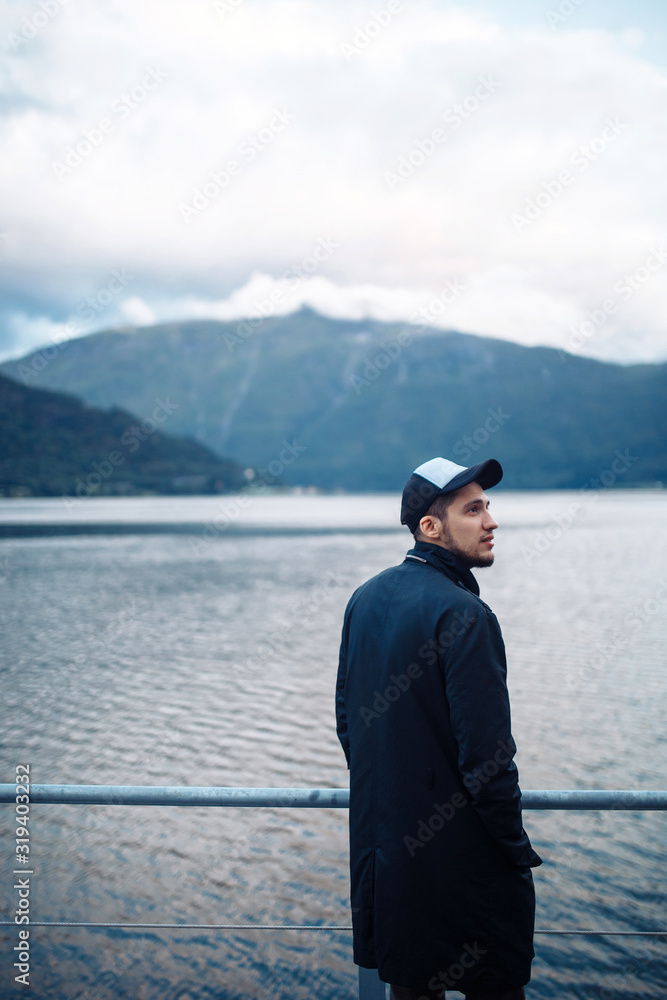 Fototapeta premium Young man posing on a background of mountains in the Norway. Man tourist hiking to beautiful mountain lake. Travelling, lifestyle, adventure, concept.