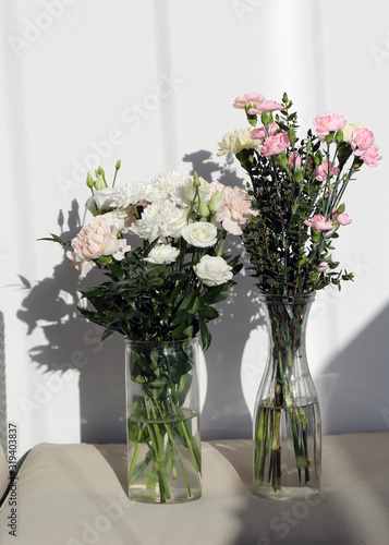 Super cute, light color flower bouquets including baby pink and white dianthus flowers with white chrysanthemum flowers, and some other white flowers. Photographed with a white wall on the background. © Nora