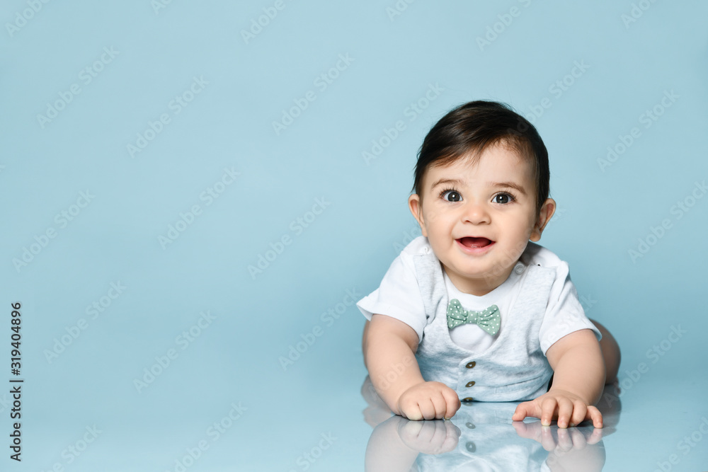 Little toddler in white bodysuit as a vest with bow-tie, barefoot. He is laying on the floor against blue background. Close up Little toddler in white bodysuit as a vest with bow-tie, barefoot. He is laying on the floor against blue background. Close up