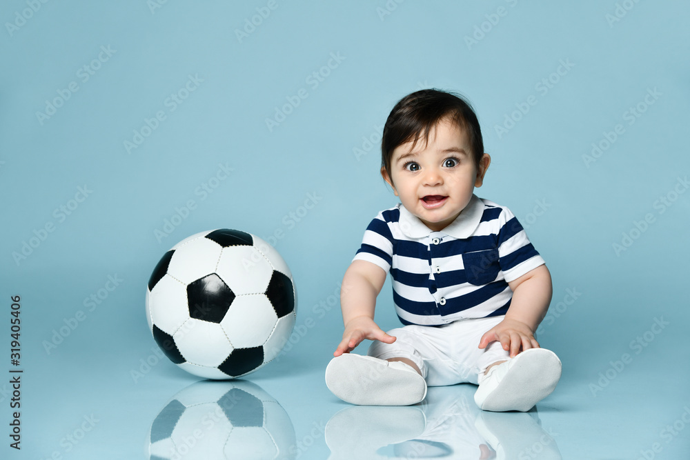Toddler in striped t-shirt, white pants and booties. He is looking up, sitting on floor against blue background. Close up Toddler in striped t-shirt, white pants and booties. He is looking up, sitting on floor against blue background. Close up