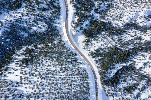 An aerial view of a highway in the forest and mountains with covered snow.