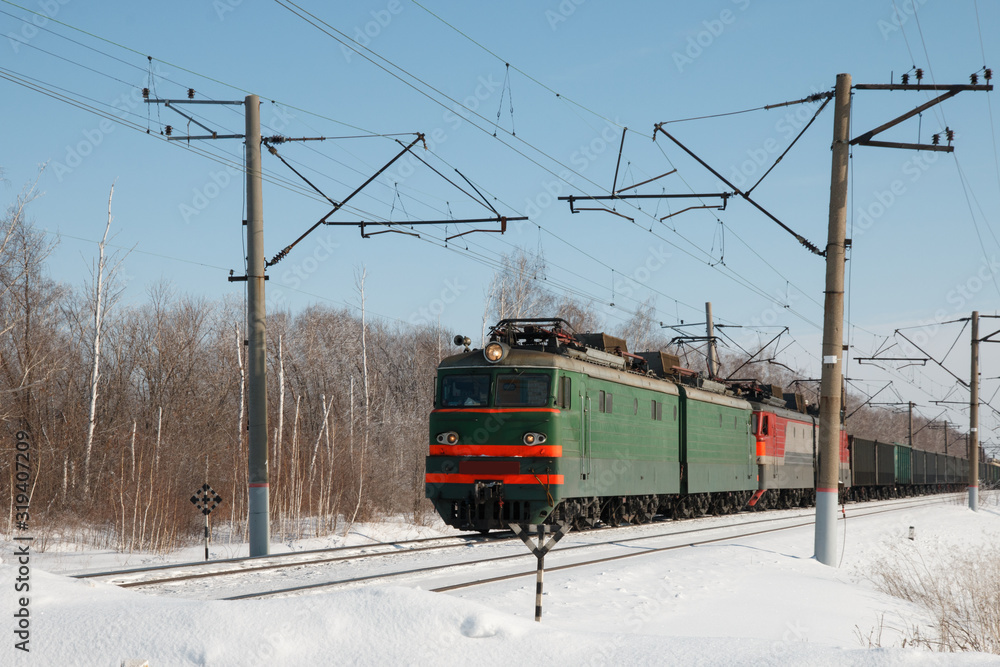 winter train leaves the forest and approaches the station crossing, railway power line