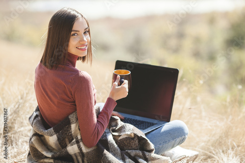 Young attractive woman working on laptop outdoors. Woman on natural background doing her freelance job on pc. Remote vorker on vacation. photo