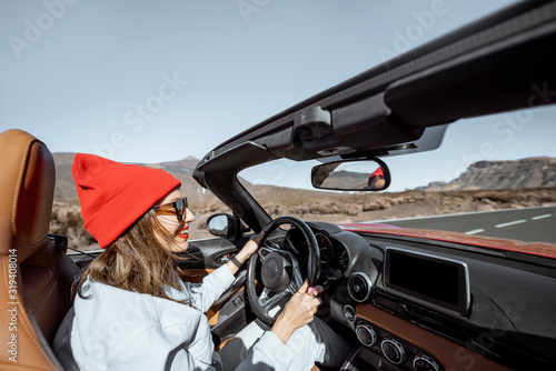 Happy woman in red hat driving convertible car while traveling on the desert road. Carefree lifestyle and travel concept