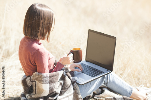 Young attractive woman working on laptop outdoors. Woman on natural background doing her freelance job on pc. Remote vorker on vacation. photo