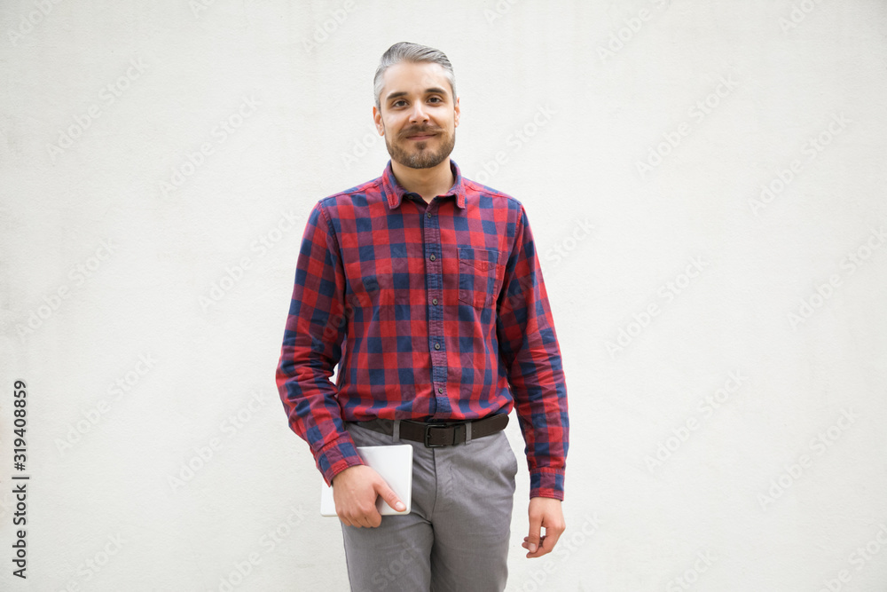 Smiling positive young man holding tablet. Cheerful bearded guy holding tablet in hand. Technology concept Smiling positive young man holding tablet. Cheerful bearded guy holding tablet in hand. Technology concept