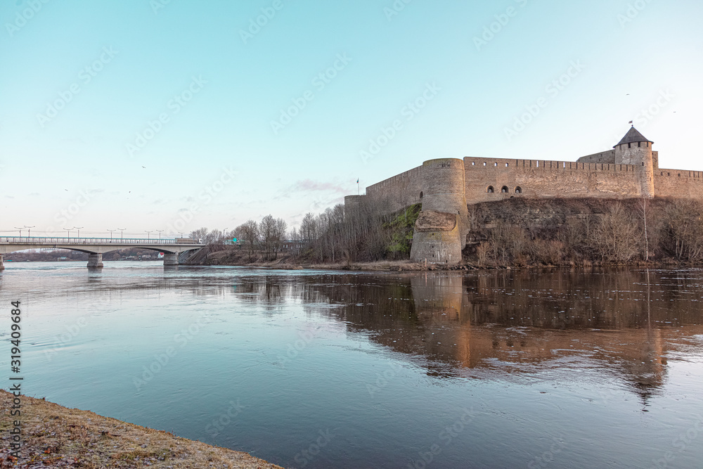 Obraz premium Beautiful river embankment overlooking the medieval castle and the fortress wall. Walk in the early morning in winter