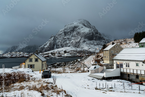 Scandinavian village with cozy houses and snowy mountain peak on horizon. Lofoten islands, Norway.