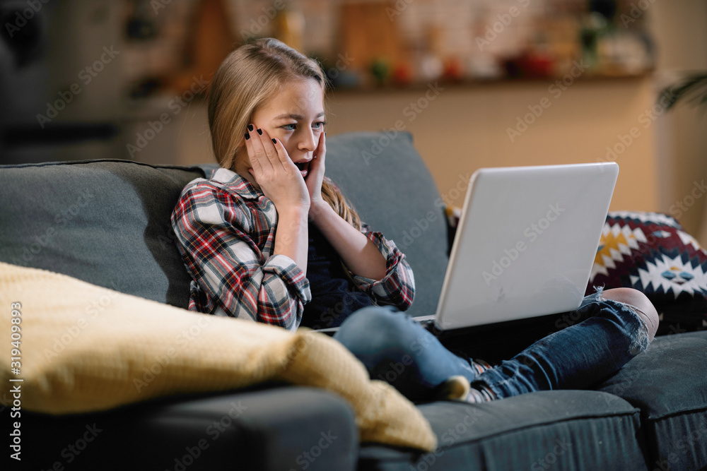 Fototapeta premium Surprised girl with laptop sitting on sofa.