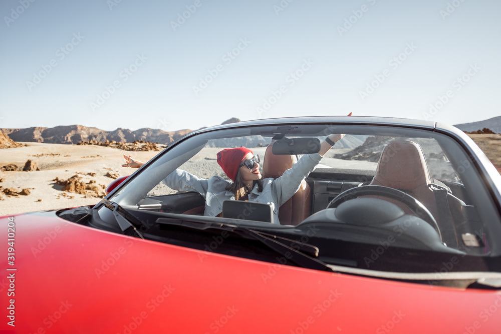 Obraz premium Young woman traveling by convertible car on the picturesquare desert valley, sitting at the passenger seat. Front view through windshield