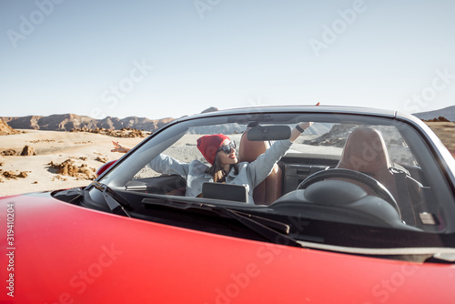 Young woman traveling by convertible car on the picturesquare desert valley, sitting at the passenger seat. Front view through windshield © rh2010