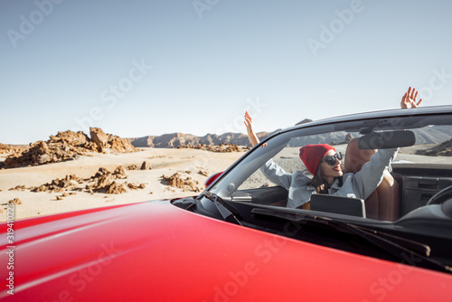 Young woman traveling by convertible car on the picturesquare desert valley, sitting at the passenger seat. Front view through windshield
