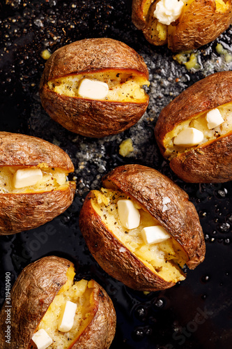 Baked potato, hot baked potatoes with the addition of butter and freshly ground black pepper and sea salt flakes on a black background, top view