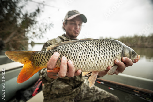 Young amateur angler holds the big Carp fish (Cyprinus carpio) being in the boat on the river