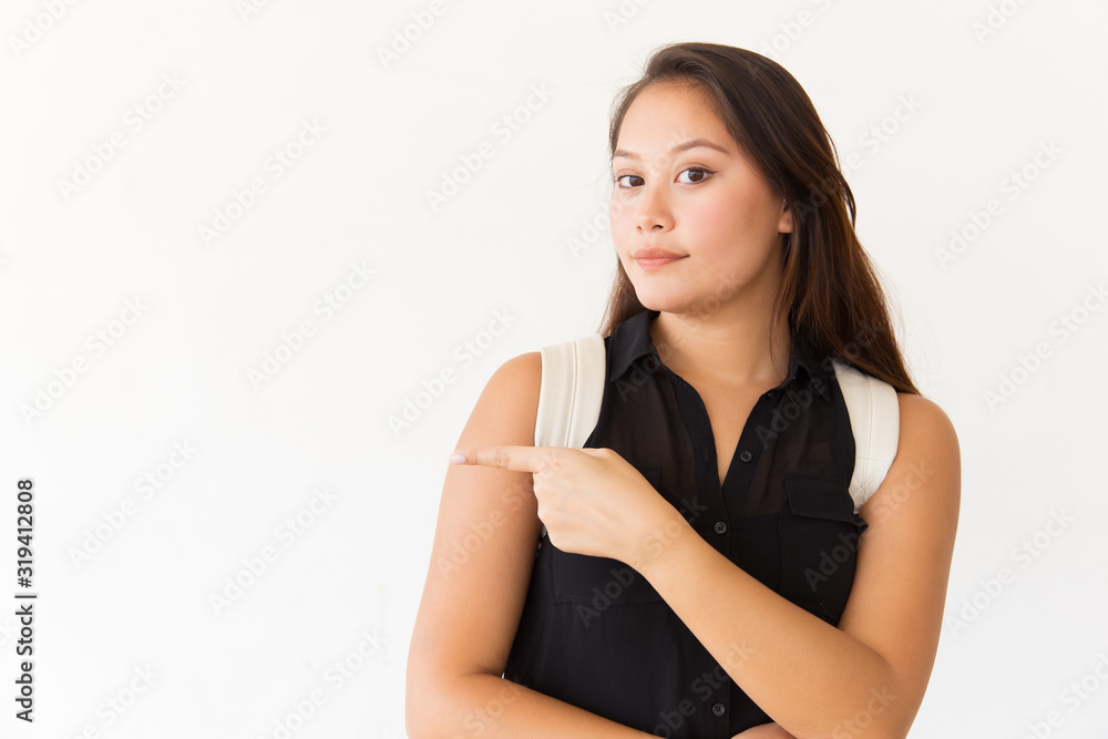 Female student pointing away with finger. Attractive young Asian woman with backpack pointing with finger and looking at camera. Advertisement concept Female student pointing away with finger. Attractive young Asian woman with backpack pointing with finger and looking at camera. Advertisement concept