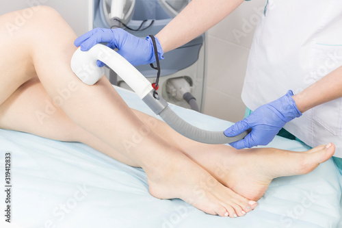 The process of laser depilation of female limbs in the beauty salon. 