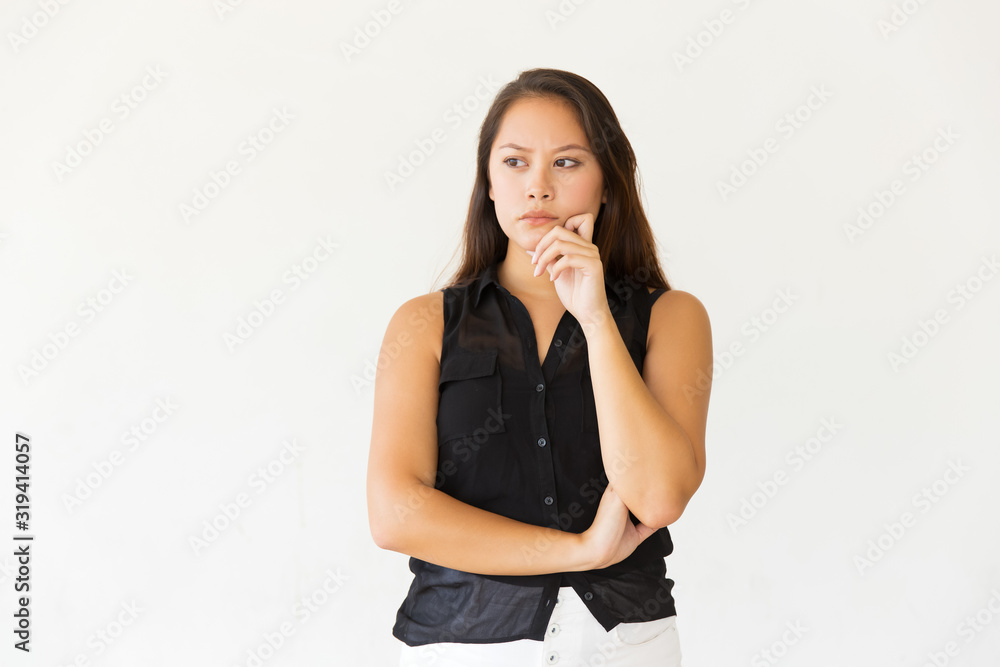 Pensive young woman with hand on chin. Portrait of serious young Asian woman standing with hand on chin and looking aside isolated on white background. Thinking concept Pensive young woman with hand on chin. Portrait of serious young Asian woman standing with hand on chin and looking aside isolated on white background. Thinking concept