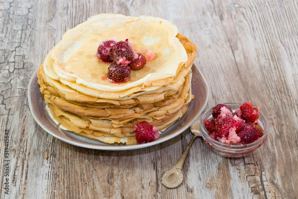 Stack of fresh homemade pancakes with red fresh strawberries in sugar in a plate on an old wooden table, vintage background, rustic style, copy space Stack of fresh homemade pancakes with red fresh strawberries in sugar in a plate on an old wooden table, vintage background, rustic style, copy space