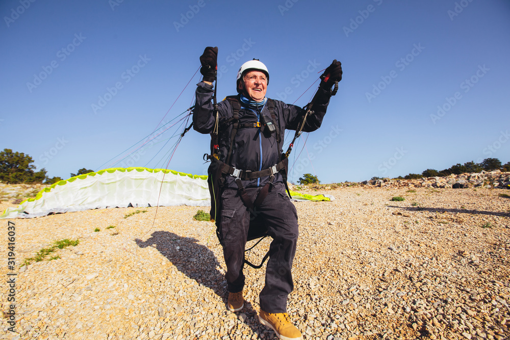 Active senior paraglider on the ground prepairs to fly. Active senior paraglider on the ground prepairs to fly.