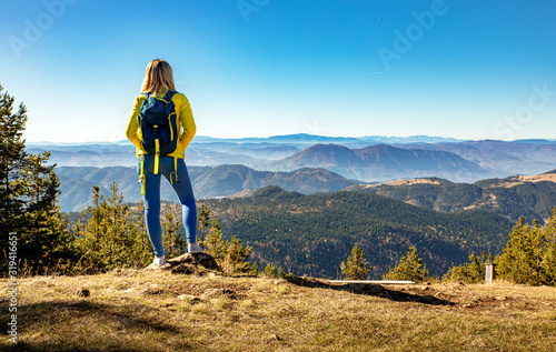 Rear view of female hiker with backpack standing on top of the mountain enjoying the view during the day. photo