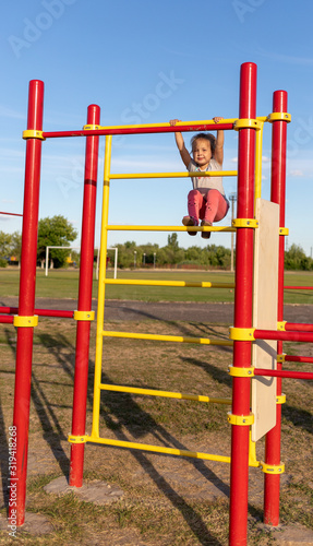A small child goes in for sports in the stadium. hanging on the horizontal bar, on the uneven bars