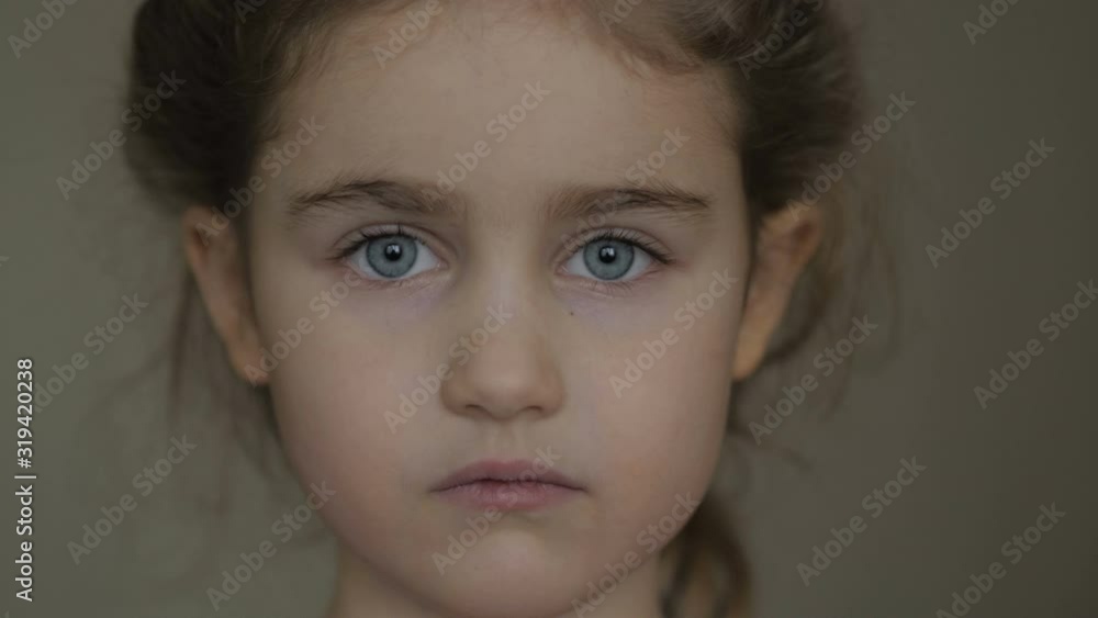 Portrait little young girl with blue eyes looking at camera. Young serious child looking at camera. Closeup. Indoors. Sad little kid girl portrait looking. Portrait little young girl with blue eyes looking at camera. Young serious child looking at camera. Closeup. Indoors. Sad little kid girl portrait looking.
