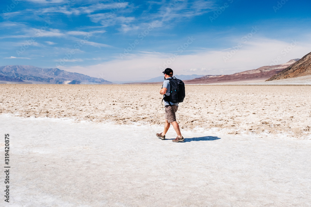 A tourist man with a hat to curb from the sun and a traveler's backpack enjoys a sunny day in the Death Valley desert
