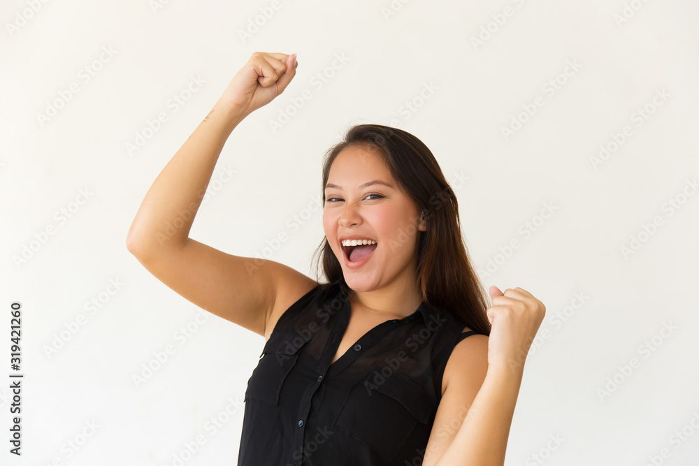 Excited young woman raising fists. Cheerful young Asian woman triumphing and celebrating success isolated on white background. Winner concept Excited young woman raising fists. Cheerful young Asian woman triumphing and celebrating success isolated on white background. Winner concept