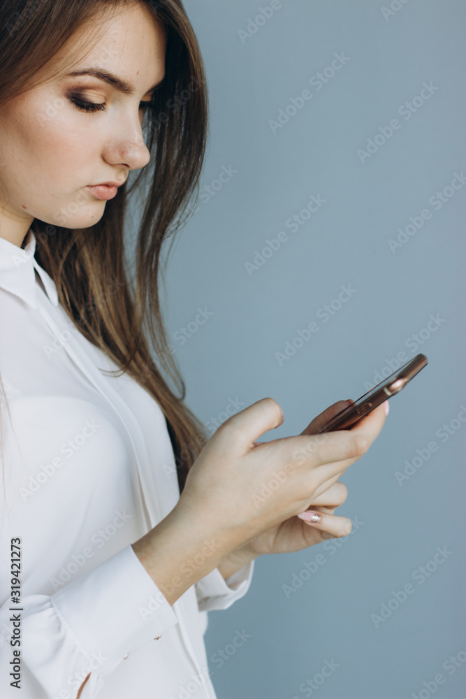 A pretty girl in a white blouse holds a smartphone. A pretty girl in a white blouse holds a smartphone.