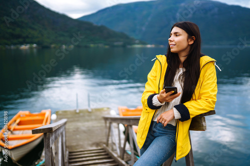 The girl tourist takes a photo on the phone by the lake in Norway. Young woman takes selfie against the backdrop of the mountains in the Norway. Travelling, lifestyle, adventure, concept. © maxbelchenko