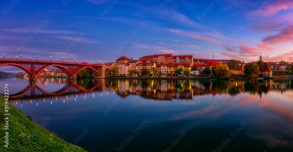 Amazing view of Maribor Old city, Main bridge (Stari most) on the Drava river before sunrise, Slovenia. Scenic cityscape with color sky and reflection, travel background for wallpaper, large panorama
