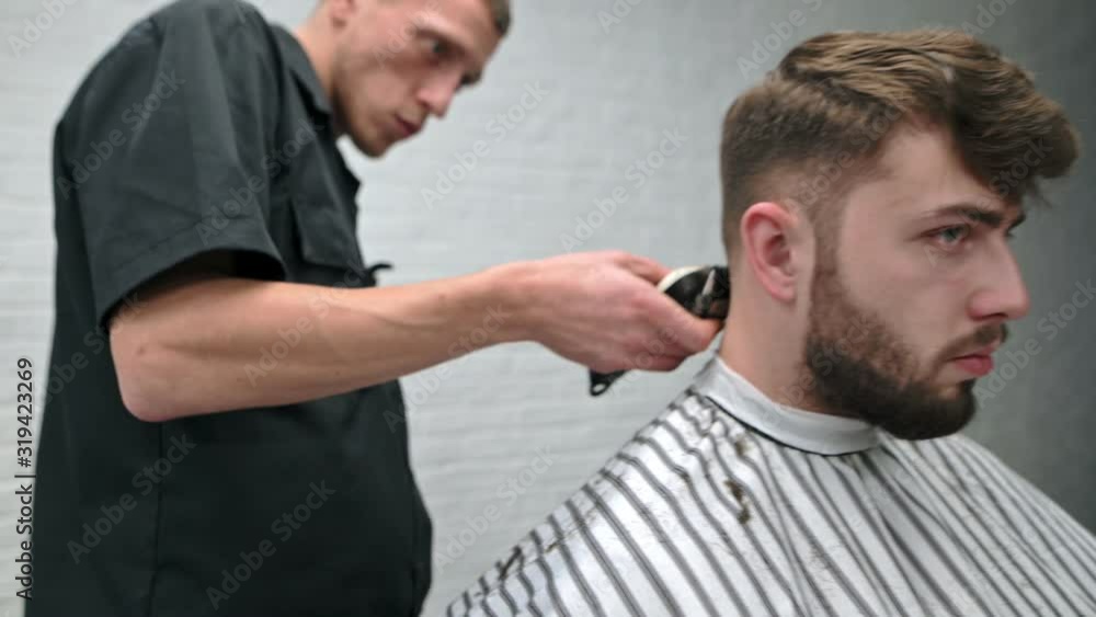 Cheerful man with a beard visits a barber shop. Barber creating a hairstyle with a clipper in his hands. Professional hairdresser makes stylish hairstyle for a beautiful client in a male hairdresser Cheerful man with a beard visits a barber shop. Barber creating a hairstyle with a clipper in his hands. Professional hairdresser makes stylish hairstyle for a beautiful client in a male hairdresser