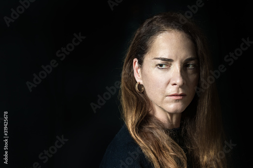 Portrait of a mature woman, pensive, looking away over black background.