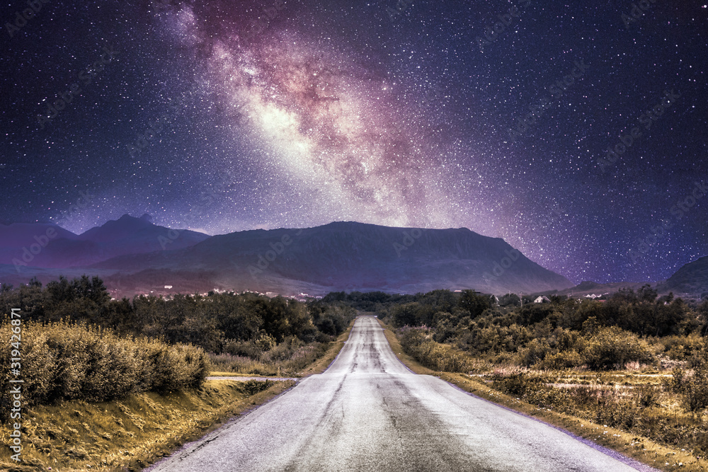 Countryside road with mountains and the milky way galaxy in the background.