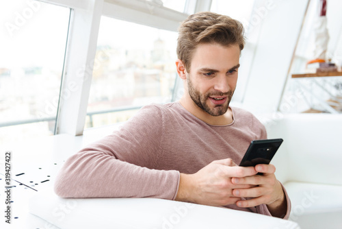 Image of young bearded man using smartphone while sitting in cafe indoors